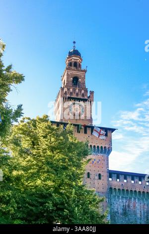 Ein großer Uhrenturm mit einer weißen und roten Flagge oben in Mailand Italien. Die Uhr befindet sich auf dem Turm und ist von weitem sichtbar. Der Turm ist s Stockfoto