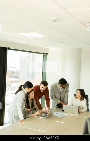 In einem eleganten Büro arbeitet eine Gruppe von Fachleuten an einem Tisch zusammen und teilt Ideen und Erkenntnisse, während sie Notebooks nutzen. Die Atmosphäre ist Stockfoto