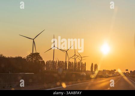 Ein wunderschöner Sonnenaufgang beleuchtet Windturbinen am Horizont und symbolisiert saubere Energie und Umweltbewusstsein Stockfoto