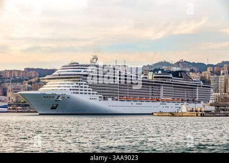 Ein großes mehrstöckiges Kreuzfahrtschiff steht am Abend im Hafen von Genua, Italien. Ein kleiner Teil der Stadt kann von hinten gesehen werden Stockfoto