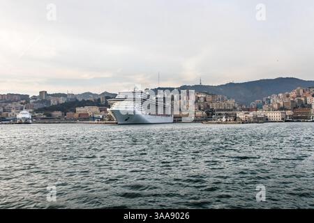 Ein großes mehrstöckiges Kreuzfahrtschiff steht am Abend im Hafen von Genua, Italien. Ein kleiner Teil der Stadt kann von hinten gesehen werden Stockfoto