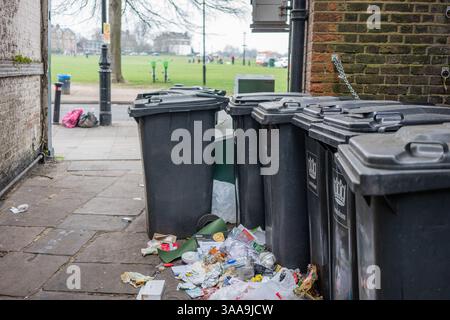 Schwarze Mülltonnen in einer Gasse im Süden Londons mit Müll auf der Straße. Stockfoto