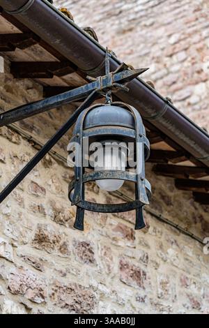 Eine Leuchte, die an einem Gebäude in Assisi in Italien Umbrien hängt. Die Leuchte besteht aus Metall und hat eine Glaskugel Stockfoto