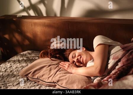 Wunderschönes glückliches Mädchen am Morgen lächelnd im Bett auf Kissen, wunderschönes Licht mit Schatten von Palmen, filmisches Bild unbeschwert glückliches Leben, ECO-f Stockfoto