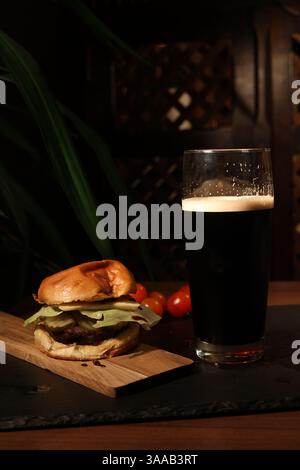 hamburger mit einem Glas frischem dunklem Bier. Mittagessen in einem Restaurant, auf dunklem Hintergrund, Beef Burger. Stockfoto