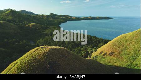 Atemberaubende Aussicht auf sanfte grüne Hügel, die auf das türkisfarbene Meer treffen und die unberührte Schönheit einer tropischen Insel im Komodo-Nationalpark in Indonesien zeigen Stockfoto