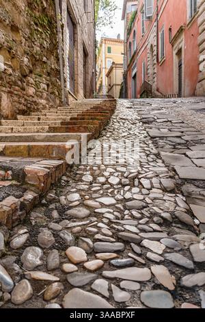 Ein Steinweg mit einer gemauerten Treppe, die in Perugia Italien Umbrien hinauf führt. Der Gehweg besteht aus Steinen und hat ein Kopfsteinpflaster-Aussehen Stockfoto