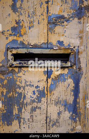Nahaufnahme einer verwitterten, abblätternden Farbe auf einer alten Holztür mit einem alten Postfach, perfekt für Hintergründe, Texturen und rustikale Designs Stockfoto