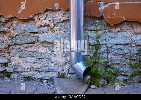 Verzinktes Metall-fallrohr gegen einen alten verwitterten Stein und eine rissige Stuckwand. Ideal für urbanen Verfall, Architektur und Textur Backgr Stockfoto
