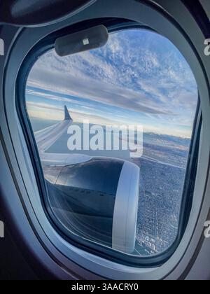 Blick aus dem Inneren eines Flugzeugs, Blick durch das Fenster auf den Flügel und den Motor über eine Küstenlandschaft. Stockfoto