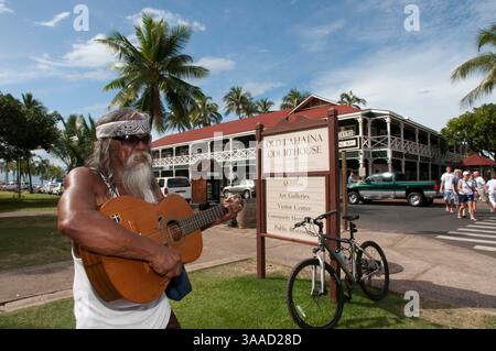 30. Dezember 2014 – Hawaii, USA – Hippye spielt Gitarre in der Nähe des emblematischen und alten Gebäudes Court and Prison of Lahaina. Maui. Hawaii. Seit seiner Eröffnung im Jahr 1860 diente das Lahaina Courthouse als Zollhaus für Walfang- und Handelsschiffe sowie als Zentrum für Regierungsämter und Gerichtsfunktionen während der Monarchie. Das „Lahaina Court & Customs House“ wurde zwischen 1858-1859 auf dem Gelände des alten Forts erbaut und wurde mit Korallenblöcken und anderen Materialien aus Kamehamehas unvollendetem Westpalast (Hale Piula) gebaut, der während eines heftigen Kauaula-Windes zerstört wurde. Th Stockfoto