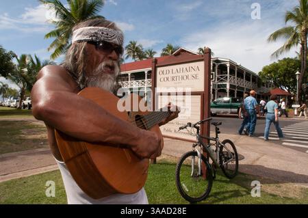 30. Dezember 2014 – Hawaii, USA – Hippye spielt Gitarre in der Nähe des emblematischen und alten Gebäudes Court and Prison of Lahaina. Maui. Hawaii. Seit seiner Eröffnung im Jahr 1860 diente das Lahaina Courthouse als Zollhaus für Walfang- und Handelsschiffe sowie als Zentrum für Regierungsämter und Gerichtsfunktionen während der Monarchie. Das „Lahaina Court & Customs House“ wurde zwischen 1858-1859 auf dem Gelände des alten Forts erbaut und wurde mit Korallenblöcken und anderen Materialien aus Kamehamehas unvollendetem Westpalast (Hale Piula) gebaut, der während eines heftigen Kauaula-Windes zerstört wurde. Th Stockfoto
