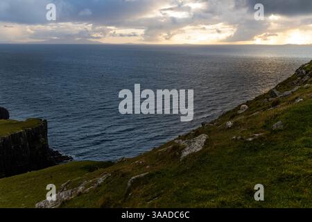 Der Neist Point bei Sonnenuntergang ist ein atemberaubender Anblick – sein Leuchtturm steht vor dramatischen Klippen, unter denen Wellen krachen. Ein Regenbogen überwölbt den Ozean Stockfoto