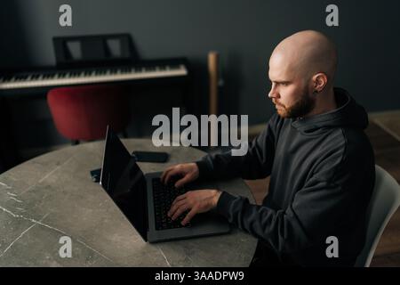Draufsicht auf einen erfahrenen Programmierer mit Bart und Hoodie, der auf einem Laptop am Tisch sitzt und sich entwickelt Stockfoto