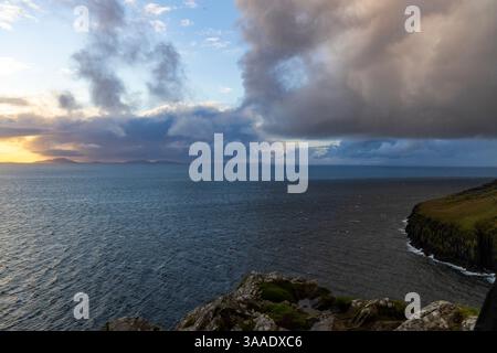 Der Neist Point bei Sonnenuntergang ist ein atemberaubender Anblick – sein Leuchtturm steht vor dramatischen Klippen, unter denen Wellen krachen. Ein Regenbogen überwölbt den Ozean Stockfoto