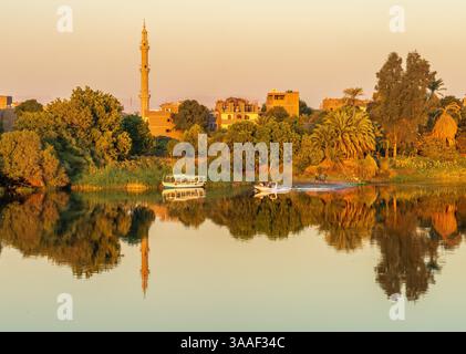 Ruhige Stadt Naqadah am Fluss in Ägypten, mit traditionellen Gebäuden und üppiger Vegetation, mit einem Polizeiboot auf dem Fluss Stockfoto