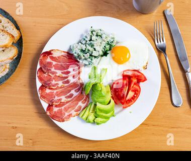 Das amerikanische Frühstück umfasst Spiegelei, Schweinespeck, Tomatenscheiben und Avocado, ergänzt durch Brot Stockfoto