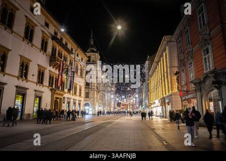 GRAZ, ÖSTERREICH - 17. DEZEMBER 2024: Abendlicher Blick auf die Herrengasse in Graz, beleuchtet von Straßenlaternen, mit Fußgängern, historisches Gebäude Stockfoto