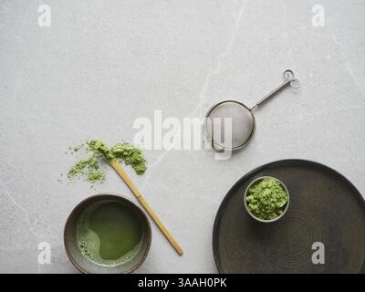 Frisch gebrühter Matcha-Grüntee-Drink zusammen mit Teepulver und Utensilien zur Zubereitung: Traditioneller Bambuslöffel und Schneebesen zusammen mit Metallsieb Stockfoto