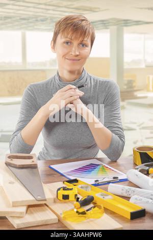 Bauarbeiterin sitzt mit Werkzeugen am Tisch Stockfoto