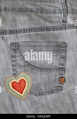 Denim-Hintergrund von grauer Farbe mit Tasche und Filzherz. Graue Textur aus Jeans. Vertikaler Hintergrund mit Denim-Textur, herzförmiger Texti Stockfoto