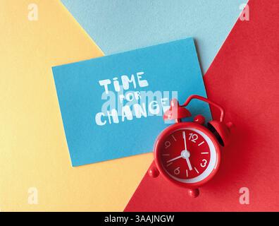 Roter Wecker und blaue Karte mit Text Time for Change auf farbenfrohem geometrischem Hintergrund, Konzept der Motivation und Transformation. Stockfoto