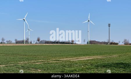 Drei veraltete Windenergieanlagen und ein Telekommunikationsmast stehen in einer grünen Agrarlandschaft in Niedersachsen, unter hellblauem Himmel, Sym Stockfoto