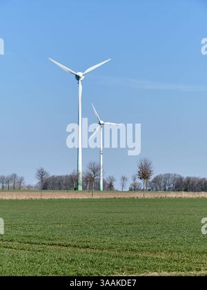 Zwei alternde Windkraftanlagen stehen in einer grünen Landwirtschaftslandschaft in Niedersachsen unter hellblauem Himmel und symbolisieren erneuerbare Energien in der Stockfoto