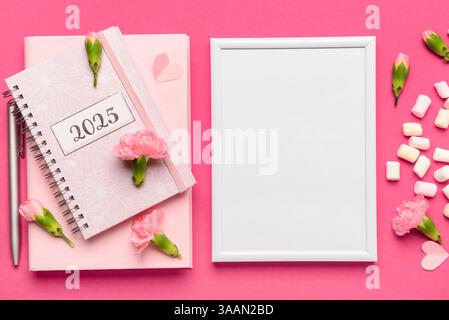 Bilderrahmen mit Notizbuch und Blumen auf rosa Hintergrund Stockfoto