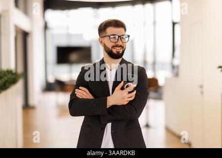 Erfolgreicher Investor arbeitet im Büro, Geschäftsmann in Business-Anzug benutzt Telefon in der Nähe von Fenstern, Mann lächelt und liest gute Nachrichten Stockfoto