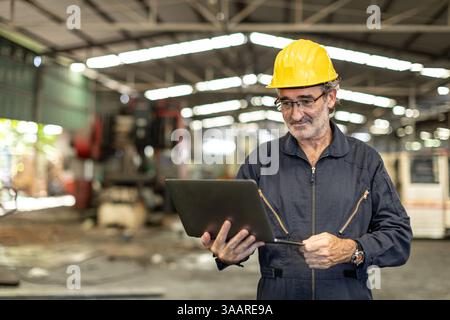 Glücklicher gesunder Senior Professional Engineer männlich, der im Lager der Schwerindustrie mit Laptop-Computer arbeitet Stockfoto