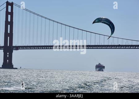 Mann, der in der Bucht von San Francisco kitesurft. Die berühmte Golden Gate Bridge in der Ferne. Beide hinterleuchtet, um Mittag aufgenommen. Kalifornien, Usa. Stockfoto