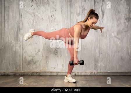 Schwangere Frau, die Hantel hebt, während sie eine einbeinige Deadlift-Übung durchführt, wodurch der aktive Lebensstil während der Schwangerschaft gefördert wird Stockfoto