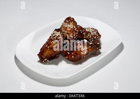 Köstliche knusprig gebratene Hähnchenflügel glasiert mit Sauce und bestreut mit Sesamsamen serviert auf weißer Keramikplatte. Stockfoto
