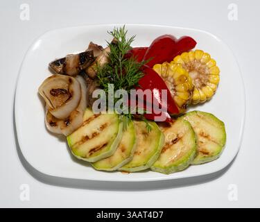 Köstliche gegrillte Gemüseplatte mit Zucchini, Mais, Pilzen, Zwiebeln, rotem Pfeffer und frischer Dill Garnish serviert auf weißer Platte. Stockfoto