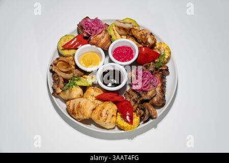 Gegrillte Fleisch- und Gemüseplatte mit Saucen auf weißer Keramikplatte. Stockfoto