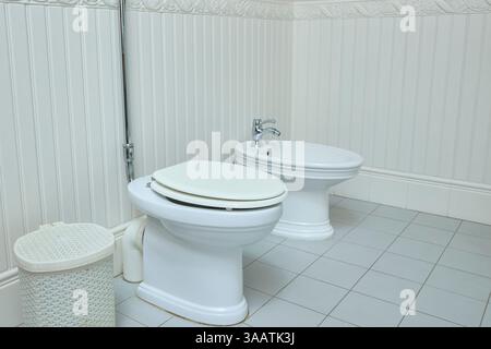 Ein sauberes Badezimmer verfügt über eine Toilette und ein Bidet nebeneinander, mit einem strukturierten Abfalleimer. Die weißen Fliesen und Wände schaffen eine schlanke und organisierte Raumumgebung Stockfoto