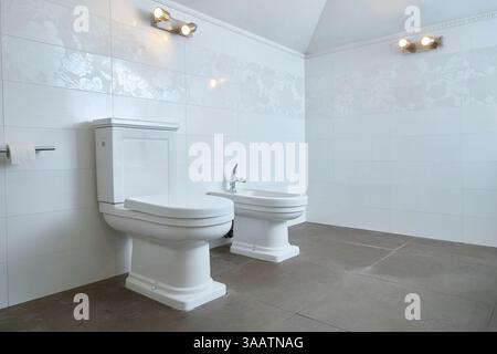 Geräumiges Bad mit weißer Keramik-Toilette und Bidet vor dem Hintergrund gefliester Wände. Elegantes und minimalistisches Design für Verachtung Stockfoto