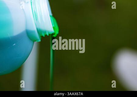 Nahaufnahme eines leuchtend grünen Waschmittels, das aus einer weißen Plastikflasche vor einem verschwommenen Hintergrund strömt. Grüne Flüssigkeit, die aus einem Behälter fließt. Kopierbereich Stockfoto