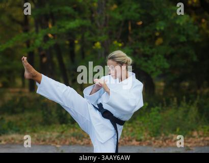 Attraktive Kämpferin in weißem Kimono mit schwarzem Gürtel tritt draußen Stockfoto