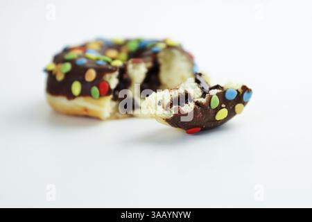 Ein gebissener Donut glasiert mit Schokolade und bunten Smarties isoliert auf weißem Hintergrund. Donut-Stücke mit bunten Schokoladenknabbern drauf. S Stockfoto
