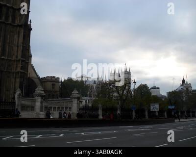 Ein Blick auf Westminster Abbey und die umliegende Architektur in London, mit einem bewölkten Himmel und Menschen, die die Straße entlang laufen. Stockfoto