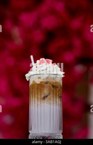 Eiskaffee mit Schlagsahne in einem Glas auf einem Hintergrund aus Blumen Stockfoto