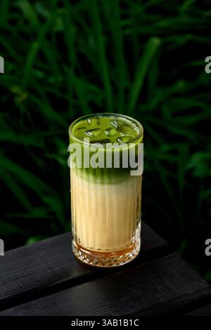 Gefrorener grüner Tee Matcha Latte in einem Glas mit grünem Hintergrund Stockfoto