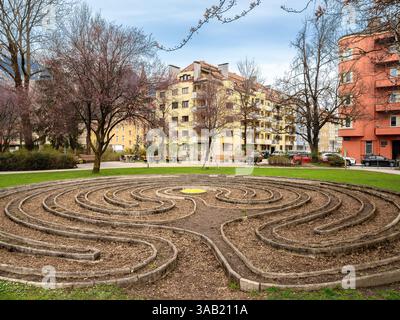 Eine ruhige Szene im Rapoldi Park in Innsbruck mit einem Labyrinth aus Steinwegen, umgeben von üppig grünen Gras und Bäumen. Im Hintergrund Stockfoto