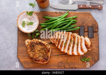 Gegrilltes Schweinekotelett oder Hühnchen in Scheiben auf einem Schneidebrett serviert mit grünen Bohnen Stockfoto