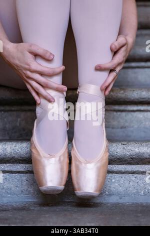 Nahaufnahme der Ballerinas auf dem Hintergrund der grauen Steinstufen. Tanzen Sie auf den Stufen. Ballerinas Füße mit pinkfarbenen Ballettpantoffeln. Minimali Stockfoto