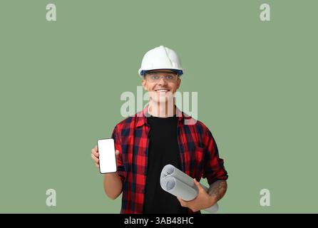 Junger männlicher Ingenieur, der einen Plan hält und ein Handy mit leerem Bildschirm auf grünem Hintergrund zeigt Stockfoto