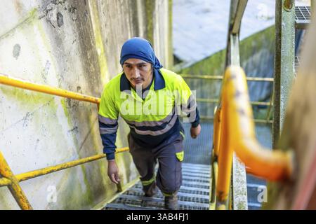 Blick von oben auf einen lateinischen Arbeiter, der die Treppe vor einem Gebäude einer Recyclinganlage hinaufging Stockfoto
