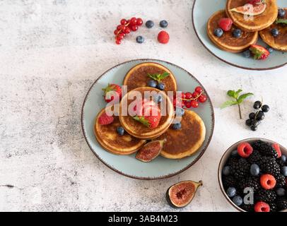 Hausgemachter Pfannkuchenstapel mit Heidelbeeren, Himbeeren und Erdbeeren auf einem weißen Teller mit einem blauen Tuch auf einer hellgrauen Tischplatte Stockfoto